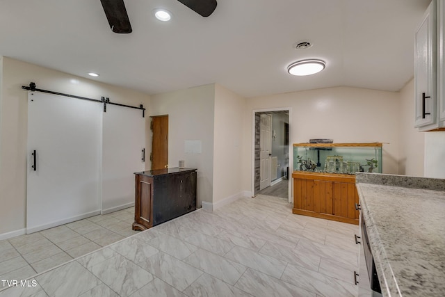 kitchen featuring lofted ceiling, white cabinetry, light stone counters, ceiling fan, and a barn door