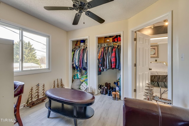 interior space with multiple closets, ceiling fan, a textured ceiling, and light hardwood / wood-style flooring