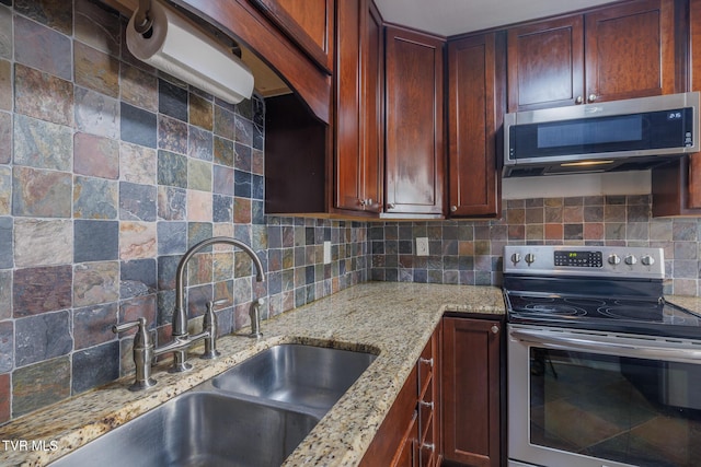 kitchen featuring stainless steel appliances, sink, light stone counters, and decorative backsplash