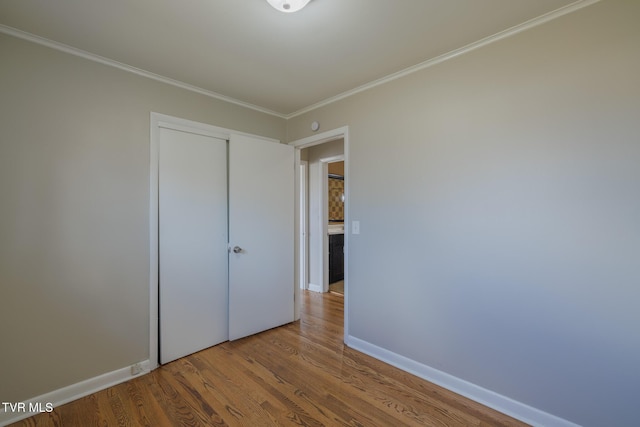 unfurnished bedroom featuring wood-type flooring, ornamental molding, and a closet