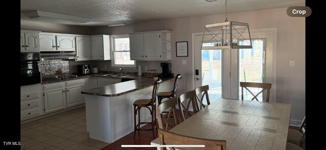 kitchen featuring white cabinets, dark countertops, a peninsula, ventilation hood, and black appliances