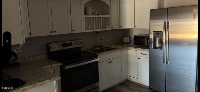 kitchen featuring light stone counters, a sink, white cabinets, appliances with stainless steel finishes, and open shelves