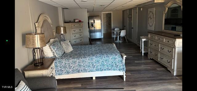 bedroom featuring dark wood-type flooring, stainless steel refrigerator with ice dispenser, and a drop ceiling