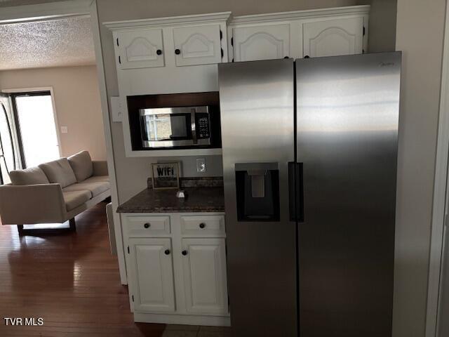 kitchen with dark wood finished floors, stainless steel appliances, white cabinetry, a textured ceiling, and dark stone countertops