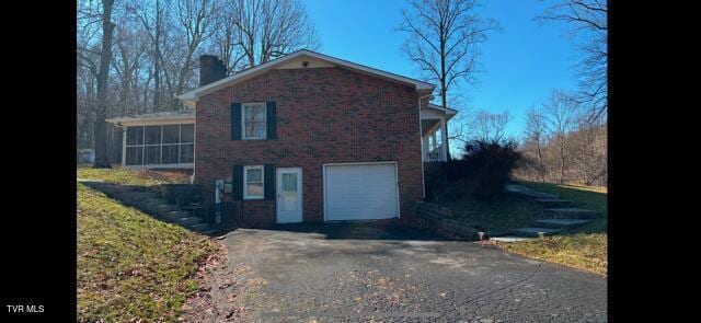 view of side of home with driveway, a garage, a sunroom, a chimney, and brick siding