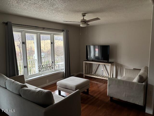 living room featuring a ceiling fan, a textured ceiling, baseboards, and wood finished floors