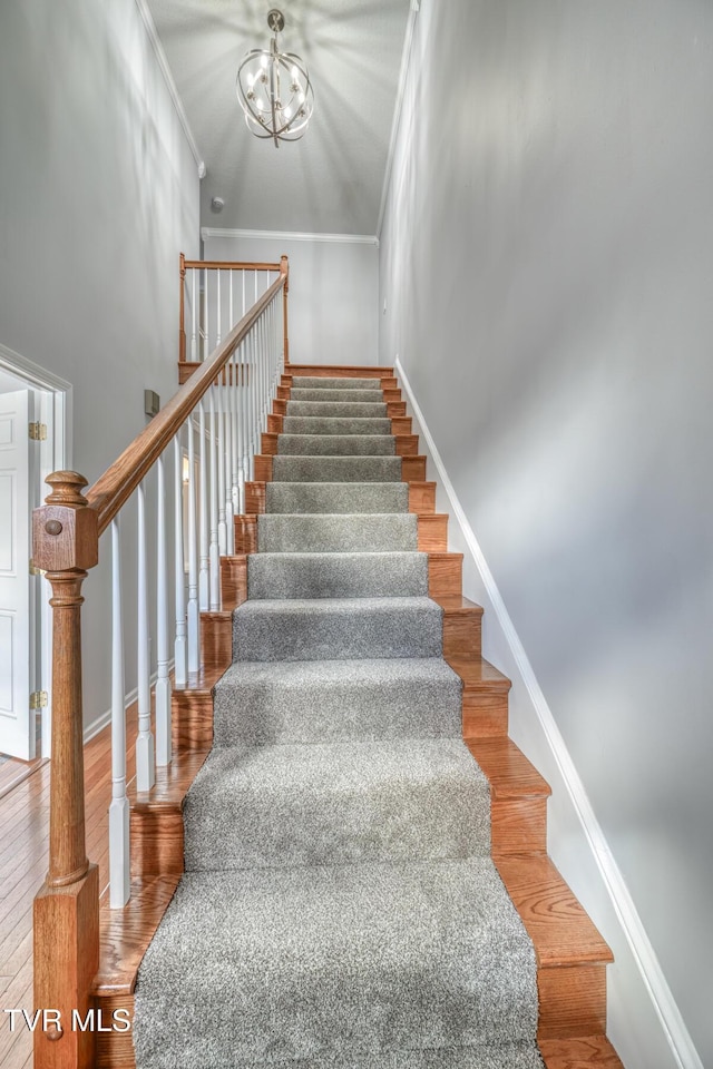 staircase featuring crown molding, wood-type flooring, and a chandelier