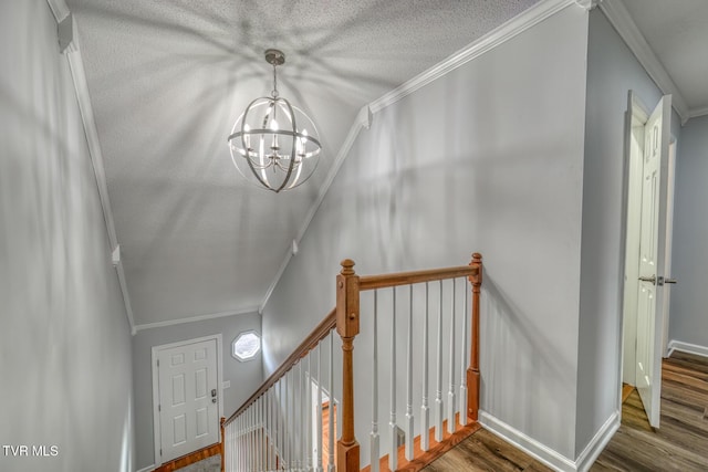 stairway featuring an inviting chandelier, crown molding, wood-type flooring, and a textured ceiling