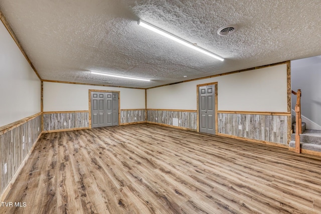 empty room featuring wood-type flooring, ornamental molding, a textured ceiling, and wood walls