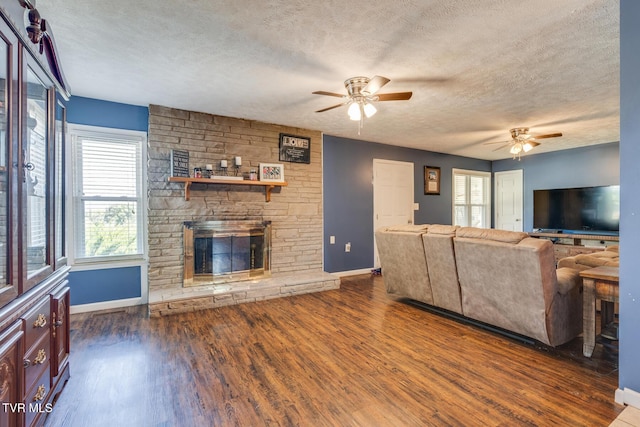 unfurnished living room featuring dark wood-type flooring, ceiling fan, a stone fireplace, and a textured ceiling