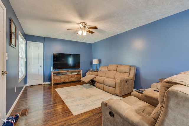 living room featuring ceiling fan, dark wood-type flooring, and a textured ceiling