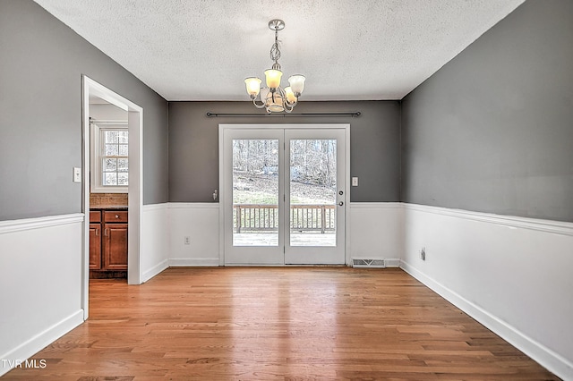 unfurnished dining area featuring a notable chandelier, light hardwood / wood-style floors, and a textured ceiling