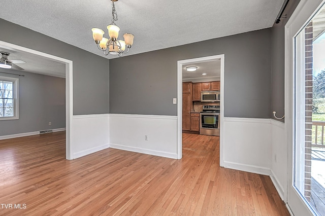 empty room with ceiling fan with notable chandelier, a textured ceiling, and light hardwood / wood-style flooring