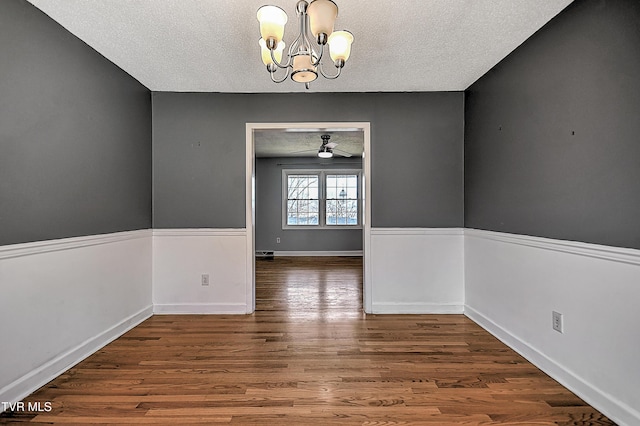 unfurnished dining area with wood-type flooring, ceiling fan with notable chandelier, and a textured ceiling