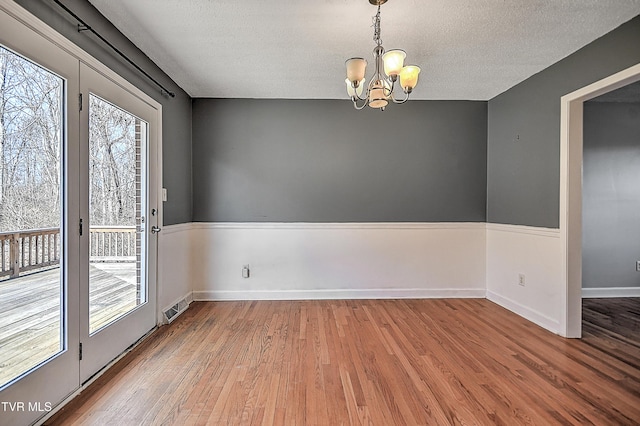 unfurnished dining area with wood-type flooring, a chandelier, and a textured ceiling