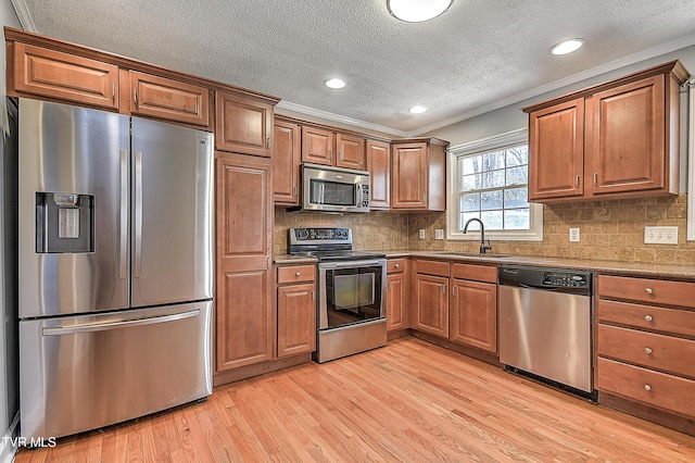 kitchen with stainless steel appliances, crown molding, sink, and light wood-type flooring