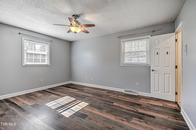 empty room featuring dark wood-type flooring, a textured ceiling, and a wealth of natural light