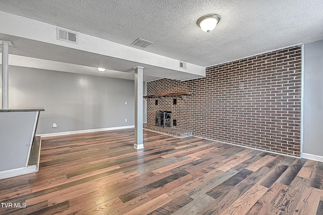 basement featuring brick wall, dark hardwood / wood-style flooring, a textured ceiling, and a wood stove