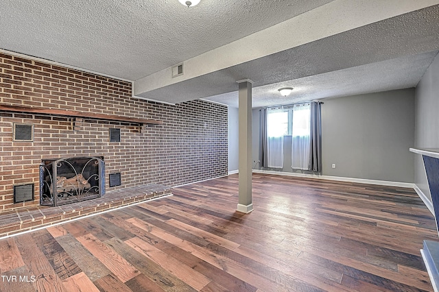 unfurnished living room with hardwood / wood-style floors, a fireplace, a textured ceiling, and brick wall