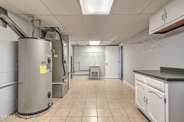 interior space with water heater, a paneled ceiling, sink, and light tile patterned floors