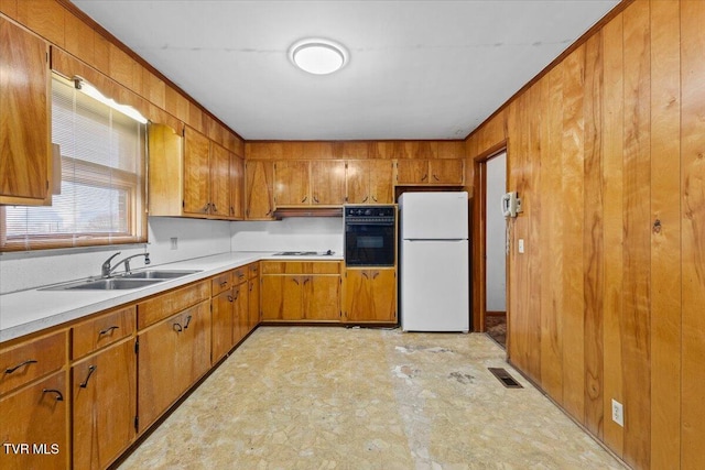 kitchen featuring wooden walls, sink, black oven, and white fridge