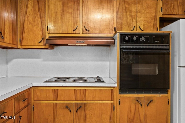 kitchen with white refrigerator, electric stovetop, oven, and range hood