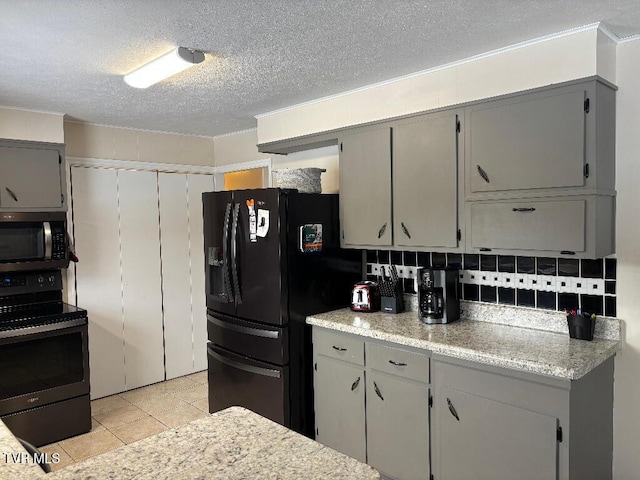 kitchen featuring gray cabinetry, light tile patterned flooring, tasteful backsplash, and black appliances