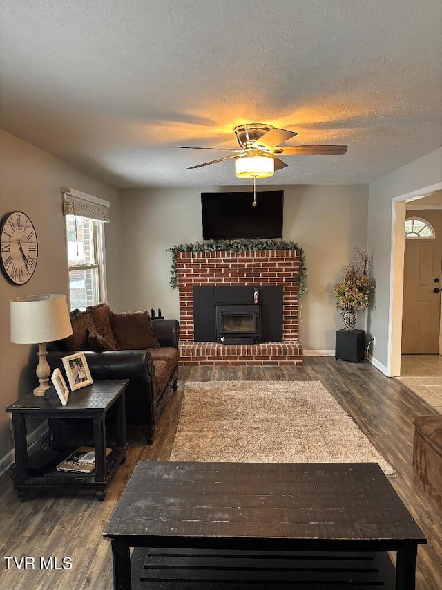 living room featuring ceiling fan, wood-type flooring, a brick fireplace, and a textured ceiling