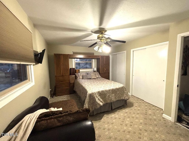 carpeted bedroom with ceiling fan, a textured ceiling, and two closets