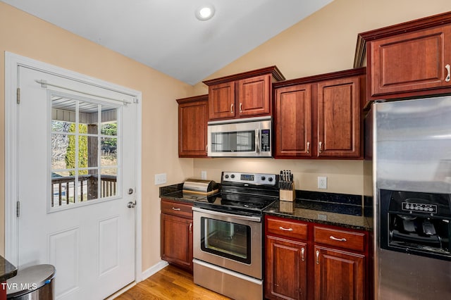 kitchen featuring lofted ceiling, light hardwood / wood-style flooring, stainless steel appliances, and dark stone counters