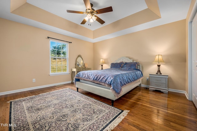 bedroom with dark hardwood / wood-style floors, ceiling fan, and a tray ceiling