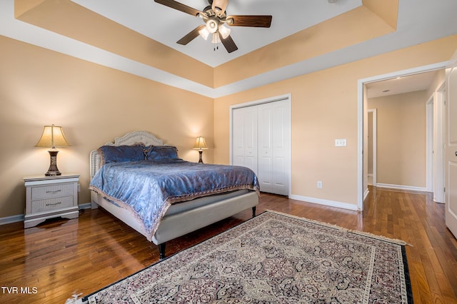 bedroom with a raised ceiling, dark hardwood / wood-style floors, ceiling fan, and a closet