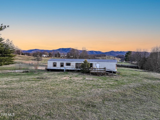 back house at dusk featuring a yard, a deck with mountain view, and a rural view