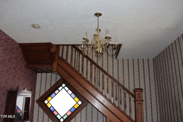 staircase with an inviting chandelier and a textured ceiling