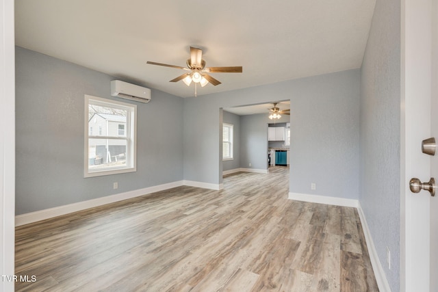 empty room featuring a wall mounted air conditioner, plenty of natural light, light hardwood / wood-style floors, and ceiling fan