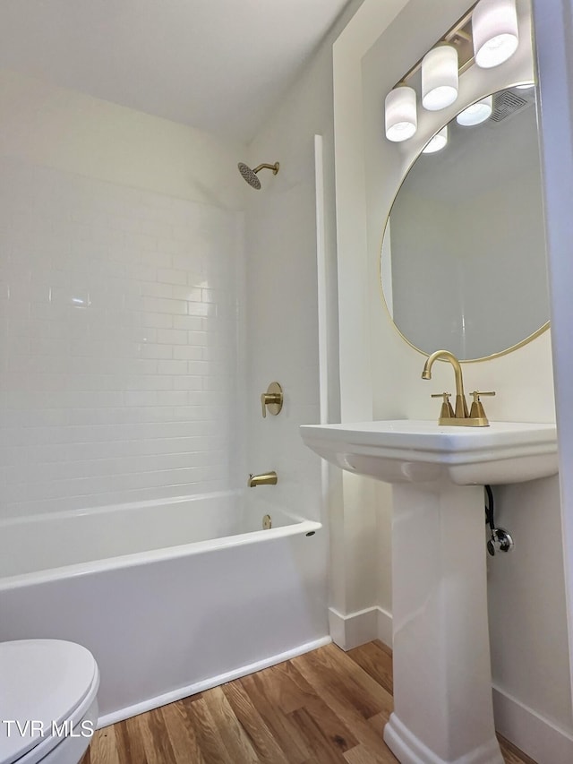 bathroom with hardwood / wood-style flooring, tiled shower / bath, and toilet