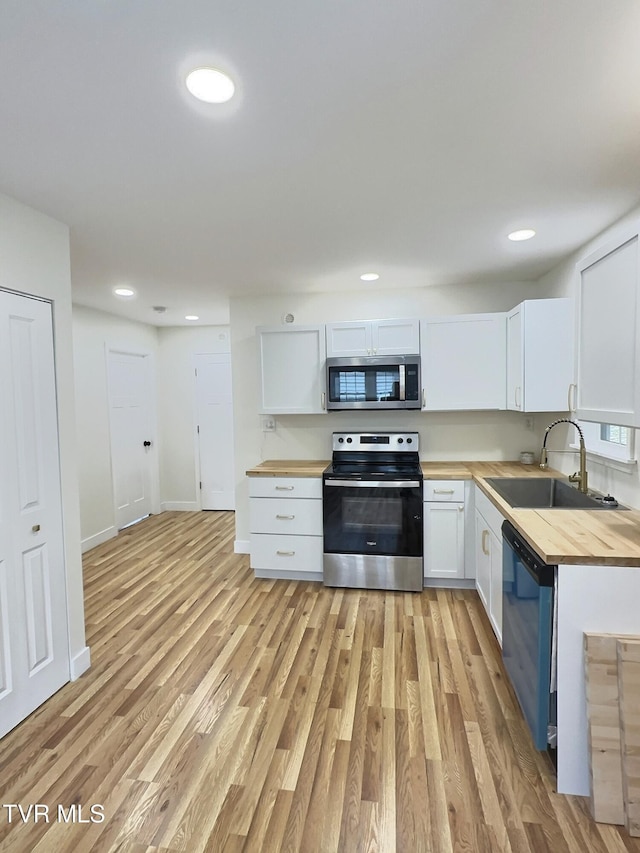 kitchen with butcher block counters, sink, white cabinetry, stainless steel appliances, and light hardwood / wood-style floors