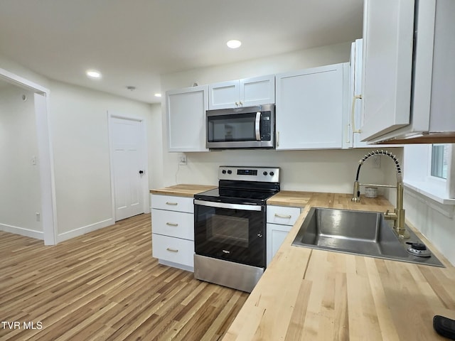 kitchen with wood counters, sink, white cabinetry, stainless steel appliances, and light hardwood / wood-style floors