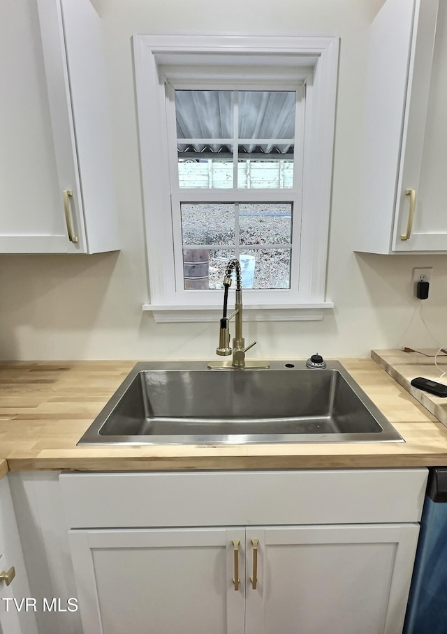 interior details featuring dishwasher, white cabinetry, sink, and wood counters