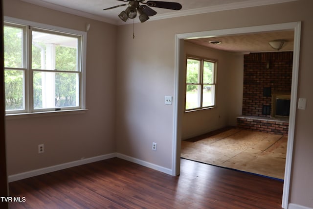 unfurnished room with dark hardwood / wood-style flooring, a fireplace, ornamental molding, and a healthy amount of sunlight