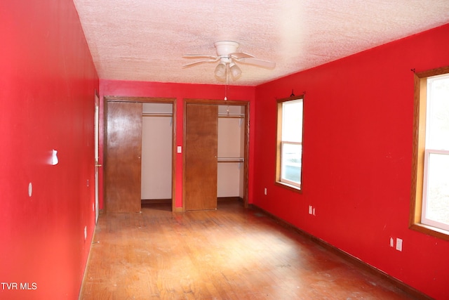 unfurnished bedroom with multiple closets, light wood-type flooring, a textured ceiling, and multiple windows