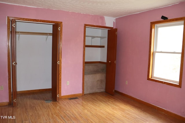 unfurnished bedroom with multiple windows, a textured ceiling, light hardwood / wood-style floors, and multiple closets