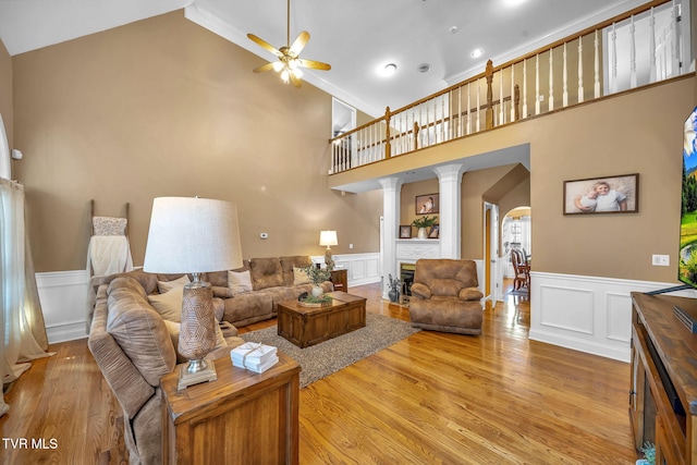 living area with arched walkways, a wainscoted wall, light wood-type flooring, and a ceiling fan