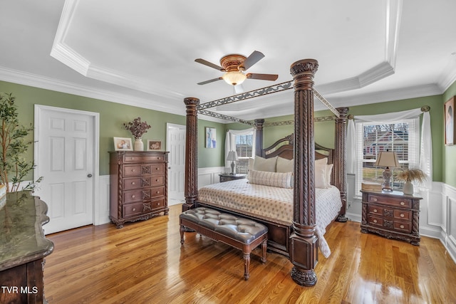 bedroom featuring light wood-style flooring, multiple windows, a tray ceiling, and wainscoting