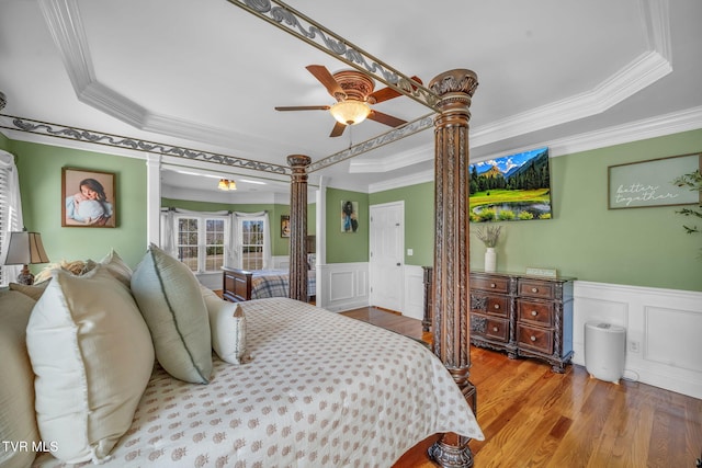 bedroom with light wood-style floors, a tray ceiling, and wainscoting