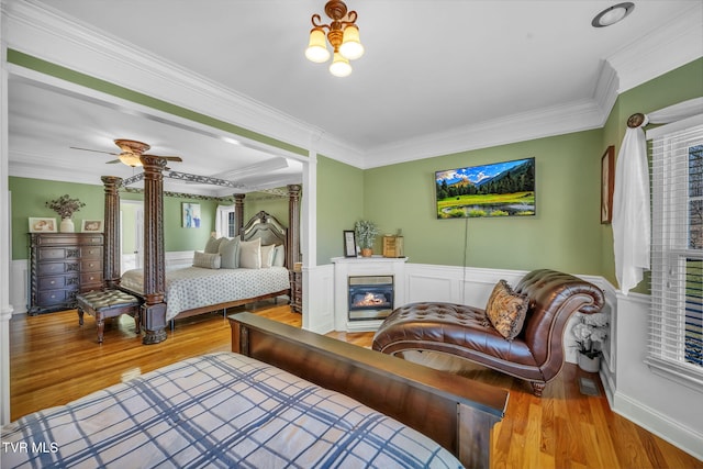 bedroom featuring light wood-style floors, crown molding, a wainscoted wall, and a glass covered fireplace