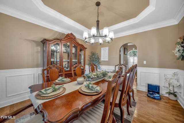 dining area with light wood-type flooring, arched walkways, a chandelier, and a tray ceiling