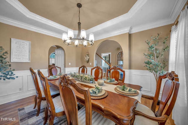 dining room featuring an inviting chandelier, a tray ceiling, arched walkways, and wood finished floors