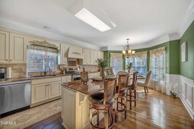 kitchen with a center island, cream cabinets, appliances with stainless steel finishes, a sink, and premium range hood