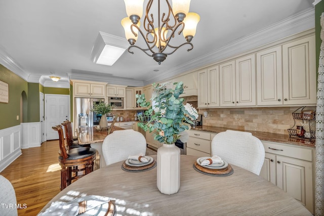 dining room featuring arched walkways, a notable chandelier, wainscoting, light wood-type flooring, and crown molding